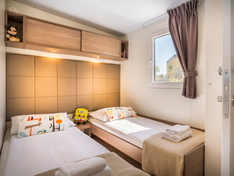 Moderne lodgekamer met twee eenpersoonsbedden, knuffels, kleurrijke kussens en opgevouwen handdoeken.