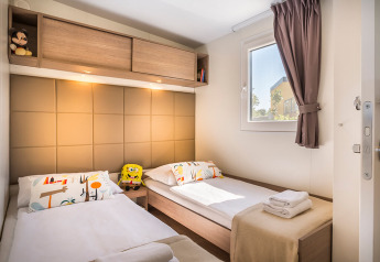 Camera di lodge moderna con due letti singoli, peluche, cuscini colorati e asciugamani piegati sul letto.