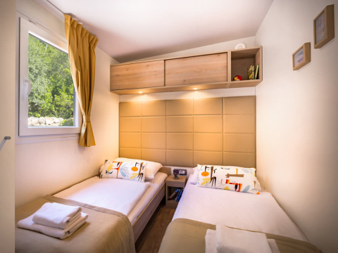 Moderne lodgekamer met twee enkele bedden, raam met gordijn, wandkasten en warme verlichting.