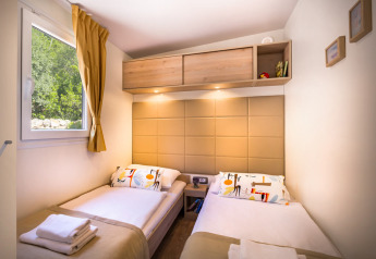 Chambre de lodge moderne avec deux lits simples, fenêtre avec rideau, rangements et éclairage chaleureux.