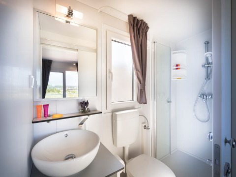 Modern lodgebadkamer met wasbak, spiegel, raam met gordijn, toilet en hoekdouche.