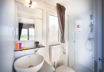 Modern lodgebadkamer met wasbak, spiegel, raam met gordijn, toilet en hoekdouche.
