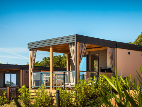 Lodge Bella Vista Chalet con terraza moderna, barandilla de vidrio y cortinas, rodeada de plantas verdes.