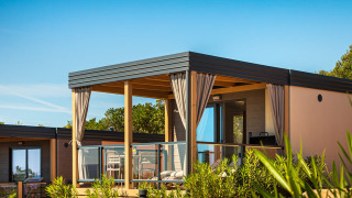 Lodge Bella Vista Chalet con terraza moderna, barandilla de vidrio y cortinas, rodeada de plantas verdes.