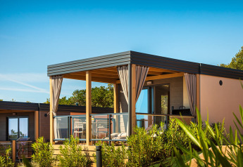 Lodge Bella Vista Chalet avec terrasse moderne, rambarde en verre et rideaux, entourée de plantes vertes.