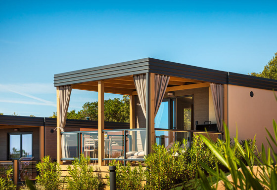 Lodge Bella Vista Chalet con terraza moderna, barandilla de vidrio y cortinas, rodeada de plantas verdes.