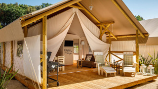Sunset Premium Glamping Tent met houten terras, luxe lounge stoelen en sfeervolle buitenomgeving.
