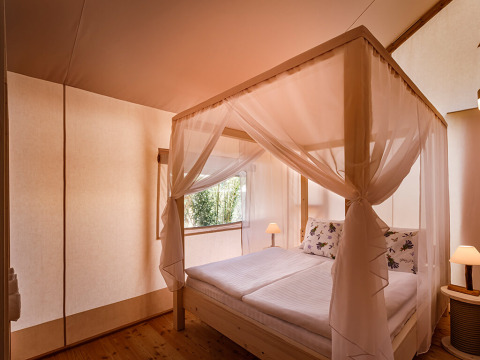 Lichte slaapkamer in de Sunset Premium Glamping Tent bij Valamar Camping Istra in Kroatië met hemelbed.