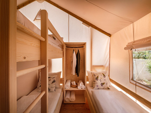 Interieur van een luxe safaritent met stapelbed, eenpersoonsbed en raam bij Valamar Camping Istra, Kroatië.