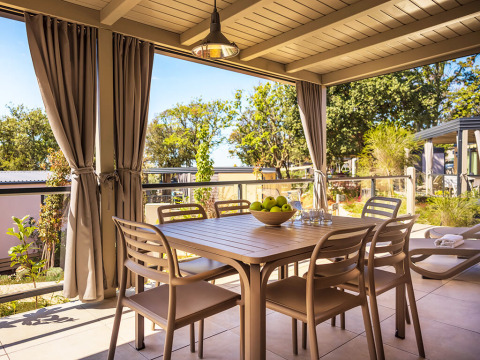 Buiten eetgedeelte bij Bella Vista Home in Valamar Camping Istra, Kroatië, met tafel, stoelen en gordijnen.