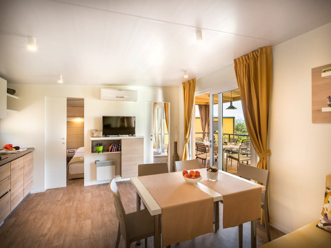 Lichte, moderne woonkamer in Bella Vista Home lodge met eettafel, tv en toegang tot terras.