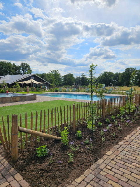 Outdoor scene near Mander, Overijssel, Netherlands, with a pool, garden, wooden fence and cloudy sky.