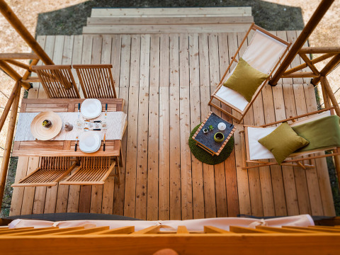 Bovenaanzicht van een houten verandaterras bij een safaritent met eetset en twee ligstoelen.