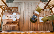 Vista aérea de una terraza de tienda safari con mesa de comedor, sillas y tumbonas de madera.