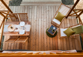 Bovenaanzicht van een houten verandaterras bij een safaritent met eetset en twee ligstoelen.
