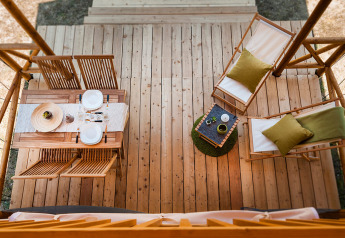Vista aérea de una terraza de tienda safari con mesa de comedor, sillas y tumbonas de madera.