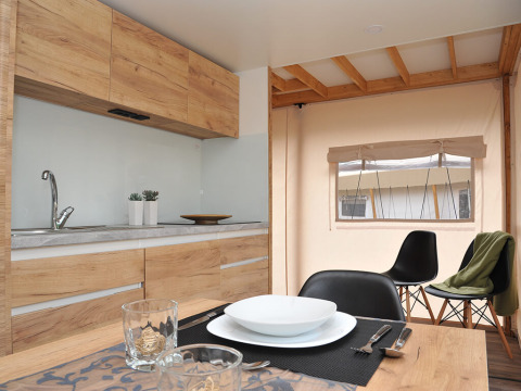 Moderne safaritent-keuken met houten kasten, gedekte eettafel en uitzicht op het raam.