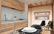 Moderne safaritentkeuken met houten kasten, opgedekte tafel en zicht op het raam binnen.