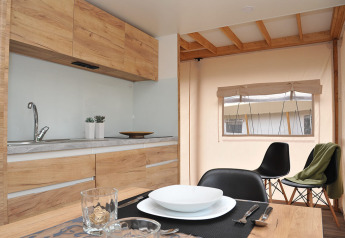 Cucina moderna in tenda safari con armadi in legno, tavolo apparecchiato e finestra panoramica.