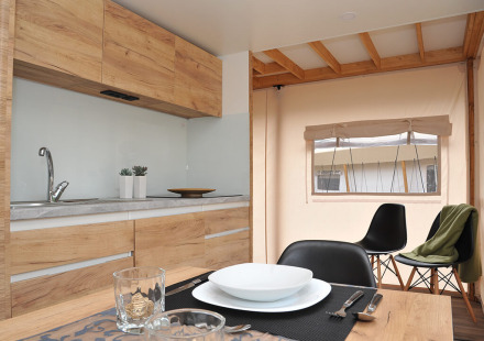 Moderne safaritent-keuken met houten kasten, gedekte eettafel en uitzicht op het raam.