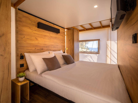 Interior view of a cozy safari tent bedroom with wooden panels, modern decor, and a window with a view.