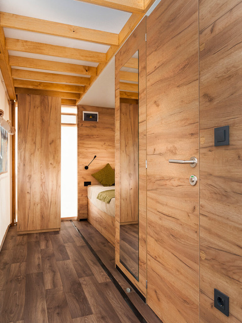 Interieur van een moderne safaritent met houten panelen, houten vloer en een gezellige slaapruimte achterin.