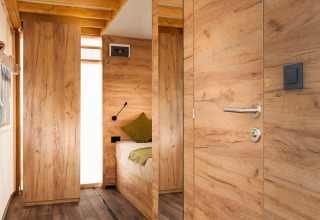 Interieur van een moderne safaritent met houten panelen, houten vloer en een gezellige slaapruimte achterin.