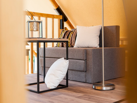 Interieur van een safaritent met een grijze bank, kussens, een modern bijzettafeltje en een lantaarn.