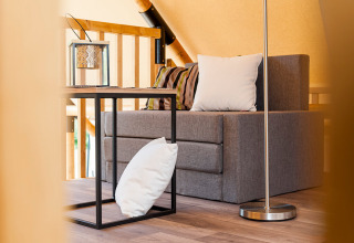 Interieur van een safaritent met een grijze bank, kussens, een modern bijzettafeltje en een lantaarn.