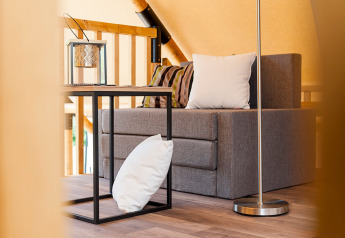 Inneneinrichtung eines Safarizeltes mit grauem Sofa, Kissen, kleinem Tisch und Laterne.