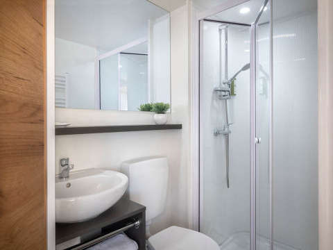Moderne badkamer in een safaritent met douche, lavabo, spiegel en toilet in een helder, net interieur.