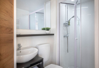 Moderne badkamer in een safaritent met douche, lavabo, spiegel en toilet in een helder, net interieur.