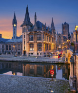 Evening view of a picturesque European city with canal and illuminated historic buildings at sunset.