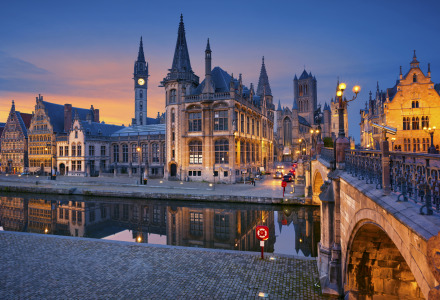 Vista nocturna de una pintoresca ciudad europea con canal y edificios históricos iluminados al atardecer.