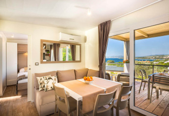 Salon moderne et lumineux d'un lodge avec coin repas, canapé et vue sur la mer depuis une grande terrasse.