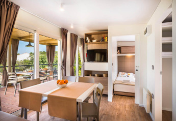 Moderne lodge leefruimte met eettafel, zicht op het terras, grote ramen, tv en toegang tot slaapkamer.