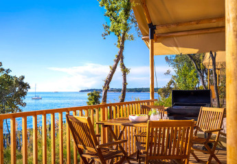 Terrazza in legno vista mare con tavolo, sedie e barbecue al Sunset Glamping Tent Seaview in Croazia.