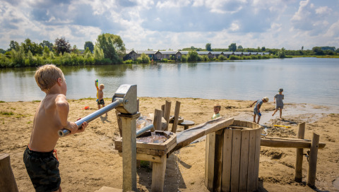 Børn leger på en sandstrand ved en sø i Familievakantiepark Krieghuusbelten i Overijssel, Holland.