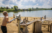 Kinder spielen am Sandstrand mit Wasserpumpe am See im Familievakantiepark Krieghuusbelten, Overijssel.
