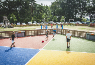 Bambini giocano a calcio su un campo colorato al parco vacanze Krieghuusbelten con parco giochi e auto sullo sfondo.