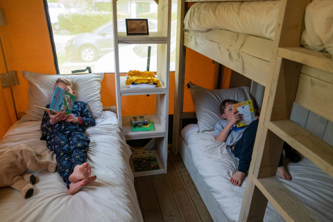 Twee kinderen lezen boeken op bedden in een Rangerlodge safaritent bij Familievakantiepark Krieghuusbelten.
