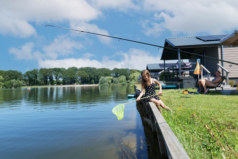 Fille pêchant au bord du lac près d'une Waterlodge au Familievakantiepark Krieghuusbelten, Pays-Bas, femme assise.