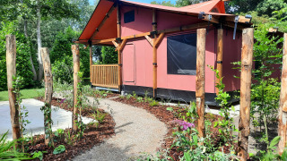Ein Kiesweg führt zu einer roten Wander Lodge mit Holzrahmen, umgeben von Garten und Bäumen.