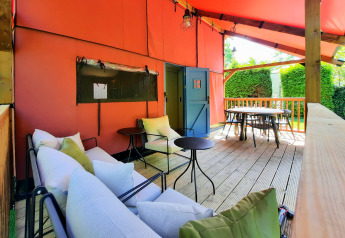 Overdækket terrasse på Wander Lodge i Vakantiepark Delftse Hout, med sofaer, borde og udsigt til haven.