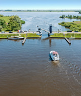 Parque vacacional junto al lago con alojamiento glamping, barcos, autos y un puente en un entorno verde.