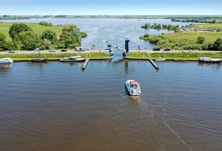 Parque vacacional junto al lago con alojamiento glamping, barcos, autos y un puente en un entorno verde.