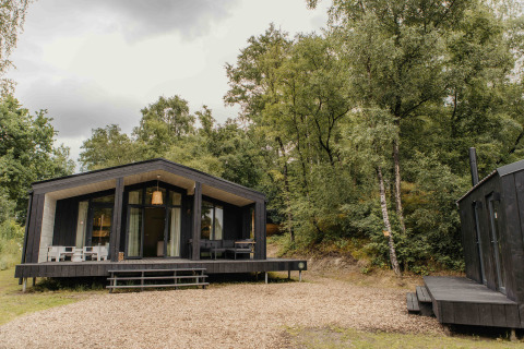 Zwart tiny house met veranda in een bos bij Wilsumer Berge, Duitsland, The Hills met hot tub en sauna.