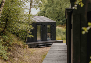 Kleine zwarte houten woning bij Wilsumer Berge, Duitsland, omringd door groen voor een rustige uitweg.