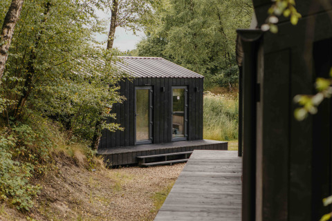 Pequeña casa negra de madera en Wilsumer Berge, Alemania, rodeada de árboles, perfecta para relajarse.