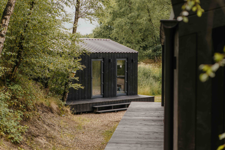 Pequeña casa negra de madera en Wilsumer Berge, Alemania, rodeada de árboles, perfecta para relajarse.